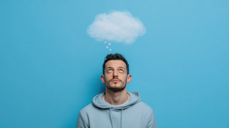 A creative concept portrait of a pensive man wearing casual clothes, cloud-shaped thought bubble hovering above him, clean modern background, no textの素材