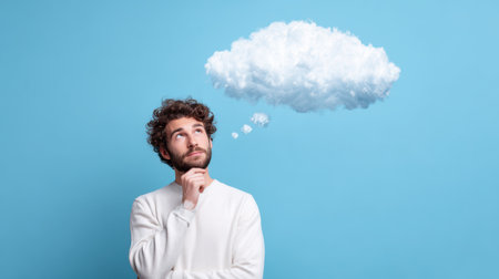 Thoughtful young man with curly hair looking up with cloud above his headの素材