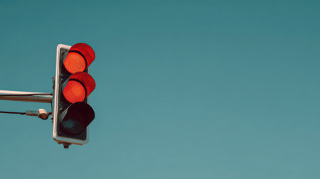 Traffic light viewed from below, red light glowing, clear sky background, geometric simplicity, no people, clean minimal feelの素材