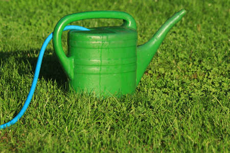 A green watering can watering the lawn during a droughtの写真素材