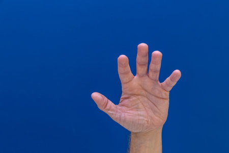 Man's hand shows five fingers on a blue background. Close-up.の写真素材