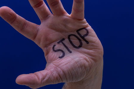 Hand with the word stop written on it against a dark blue backgroundの写真素材