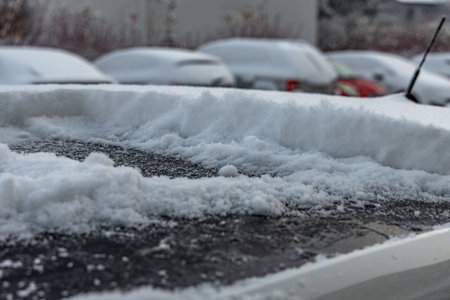 A woman shovels snow from the car, removing ice from the car body, winter attack, preparing the car for the routeの写真素材