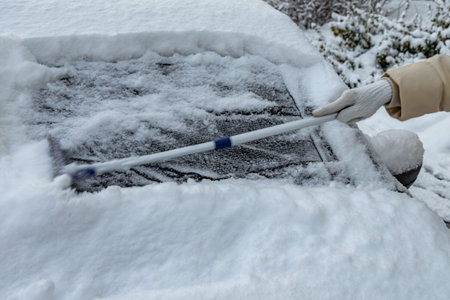 A woman shovels snow from the car, removing ice from the car body, winter attack, preparing the car for the routeの写真素材