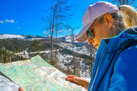 A woman in a hat and thermal jacket looks at a map looking for a way to the top of the mountainの写真素材
