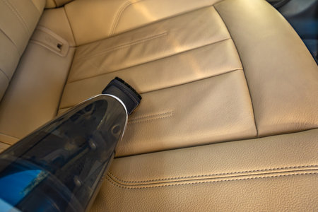 Handheld small battery-powered vacuum cleaner, cleaning rubbish in the car interior, renovating beige car seat upholsteryの写真素材