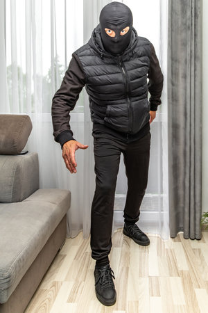 A burglar in a balaclava breaks into an apartment through the balcony, the enters the house through the windowの写真素材