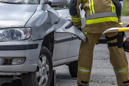 Three firefighters cut open a car after a crash during a rescue operation to pull the driver, who is trapped and unconscious, out of the car.の写真素材