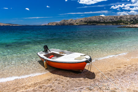 Jablanova Beach, orange fishing boat pulled up on the shore of an empty beach against the backdrop of the Adriatic Sea and Velebit Mountains on the island of KRK in Croatiaの写真素材