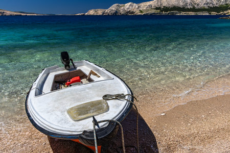 Jablanova Beach, orange fishing boat pulled up on the shore of an empty beach against the backdrop of the Adriatic Sea and Velebit Mountains on the island of KRK in Croatiaの写真素材