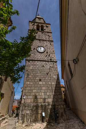 Walking among the monuments of the old town of Vrbnik, a tall tower with a clock in the center of...