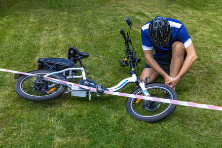 Rear view of young man sitting next to his bicycle on grassの写真素材
