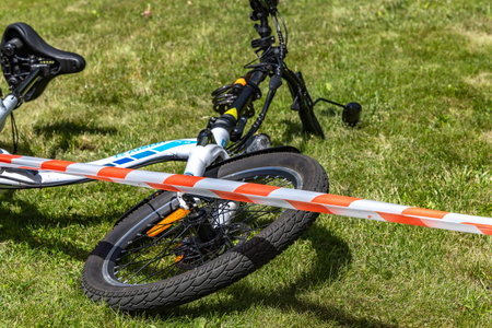 The scene of a bicycle accident surrounded by red and white warning tape, a cyclist's accident, a damaged bicycle overturned on the lawn after an accidentの写真素材