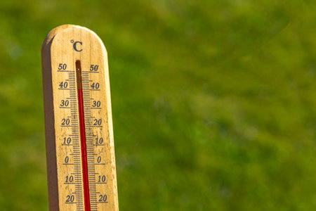 Measuring the temperature at high noon in the garden, a wooden thermometer shows a high temperature, a dangerous temperature for the grassの写真素材