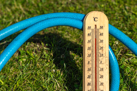 Measuring the temperature at high noon in the garden, a wooden thermometer shows a high temperature, a dangerous temperature for the grassの写真素材