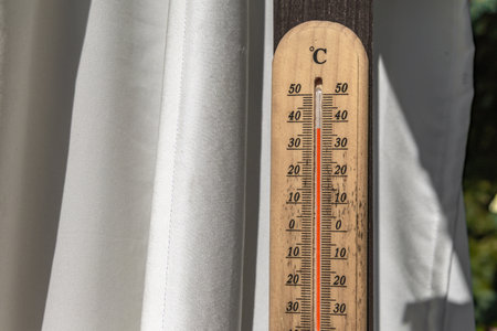 A thermometer hanging on a white curtain on a garden veranda shows extremely high summer air temperaturesの写真素材