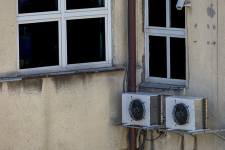Old damaged air conditioners requiring maintenance and fungicides hanging on the external wall of a public utility building, air conditioning failure,の写真素材