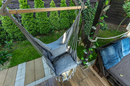 Gray fabric Brazilian chair hanging on the terrace in front of the house, garden swing, a place to relax in the shade on a hot summer dayの写真素材