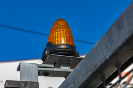 Orange warning light mounted on a metal fence, high metal fence on the boundary with an alarm system...