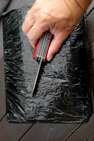 Opening a package wrapped in black stretch with a penknife, unpacking the shipment