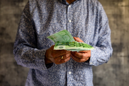 A young man, a married man in a blue elegant shirt, holds 100 euro banknotes in his hands, the man...