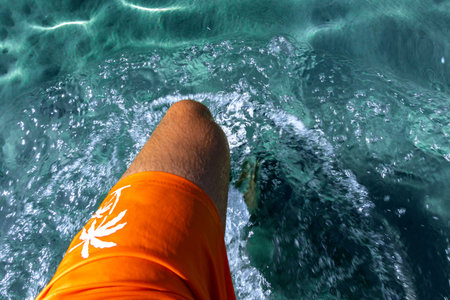 A man in orange swimming shorts walks in knee-deep water, blue water in the seaの写真素材