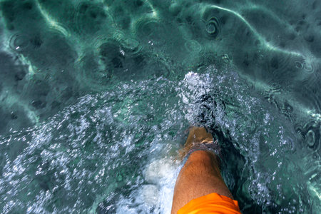 A man in orange swimming shorts walks in knee-deep water, blue water in the seaの写真素材