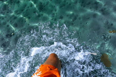 A man in orange swimming shorts walks in knee-deep water, blue water in the sea