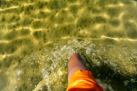 A man in orange swimming shorts walks in knee-deep water, blue water in the seaの写真素材