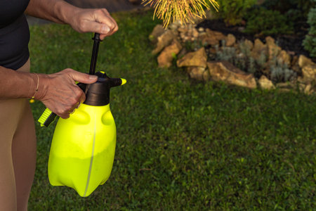 Spraying plant protection preparation in the garden, woman spraying lawn with fertilizer, yellow pressurized containerの写真素材