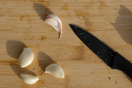 Close-up of fresh garlic cloves on a wooden cutting board with a kitchen knife, ready for cooking....