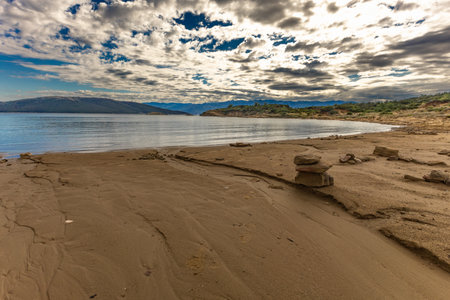 Beautiful panoramic view of a Mediterranean landscape featuring rugged rocky ground, green bushes, pine trees, and wild vegetation under a dramatic sky with scattered clouds. The scene overlooks a calm blue sea with mountains in the distance, creating a natural and serene atmosphere perfect for concepts of travel, exploration, wilderness, freedom, and untouched beauty.の写真素材