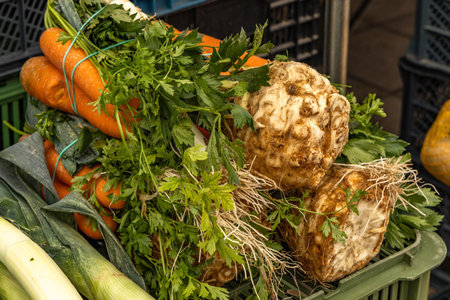 Fresh organic vegetables displayed on a market stand, including leeks, carrots, celery root and...