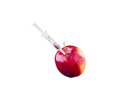 Conceptual image of a syringe injecting red liquid into a fresh apple on a white background, symbolizing GMO, biotechnology, food modification, and scientific experimentation.の写真素材