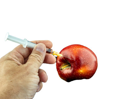 Conceptual image of a syringe injecting red liquid into a fresh apple on a white background, symbolizing GMO, biotechnology, food modification, and scientific experimentation.の写真素材