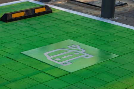 Green-painted parking spot designated for electric vehicles with EV and charging symbol on the pavement. Concept of sustainable transport, eco mobility, and modern city infrastructure.の写真素材