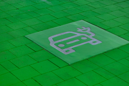 Green-painted parking spot designated for electric vehicles with EV and charging symbol on the pavement. Concept of sustainable transport, eco mobility, and modern city infrastructure.の写真素材