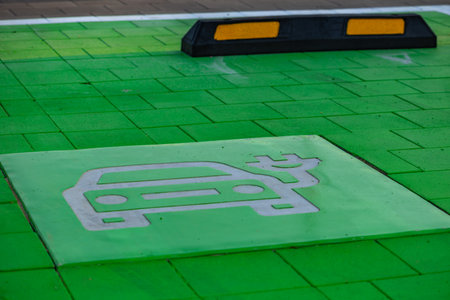 Green-painted parking spot designated for electric vehicles with EV and charging symbol on the pavement. Concept of sustainable transport, eco mobility, and modern city infrastructure.の写真素材