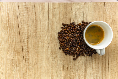 Top view of a coffee cup surrounded by spilled coffee beans on a wooden surface. Symbol of rising coffee prices, inflation, and global market trends in the coffee industry.の写真素材