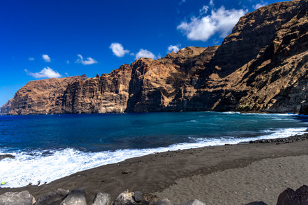 Stunning landscape of Los Gigantes cliffs on Tenerife, Canary Islands, with a rocky slope above the deep blue Atlantic Ocean under a partly cloudy sky. Travel, nature, and adventure concept.の写真素材