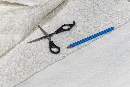 Scissors and pencil on white bouclÃ© fabric during measuring and cutting process for sewing a new sofa cover. Concept of DIY upholstery and home renovationの写真素材
