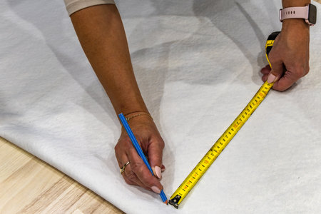 Scissors and pencil on white bouclÃ© fabric during measuring and cutting process for sewing a new...