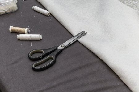 Close up of boucle fabric with scissors, thread spools, and a needle on a flat surface. Concept of upholstery sewing, handmade work, and furniture design.の写真素材