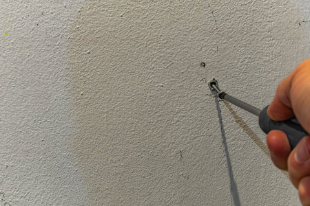 Male hand using a screwdriver to fasten a screw into a wall anchor. Close up of handyman at work, performing home repair, installation or DIY renovation on a white wall background.の写真素材