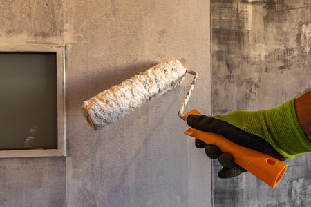 hand in glove painting the wall with orange paint roller in new houseの写真素材