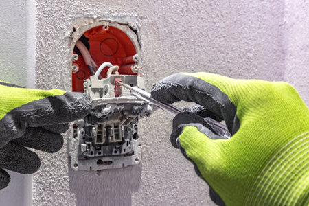 Repairing a damaged light switch, an electrician wearing protective gloves unscrews the switch...