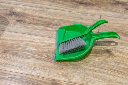 Green broom and dustpan placed on brown vinyl flooring in an apartmentの写真素材