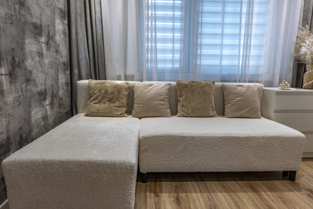 A white sofa made of elegant bouclÃ© fabric in the living room of a block of flats with pillows...