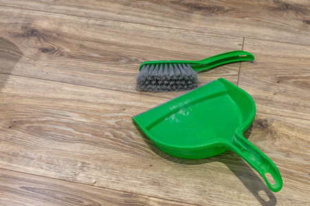 Green broom and dustpan placed on brown vinyl flooring in an apartment, cleaning the apartment after renovationの写真素材