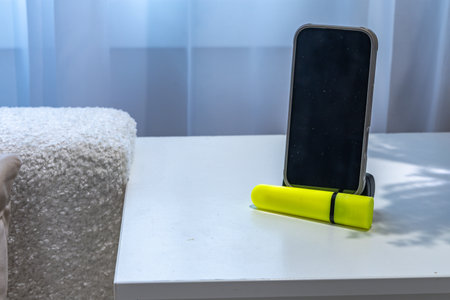 A cell phone with the display turned off is placed on a white cabinet next to a fluorescent marker.の写真素材